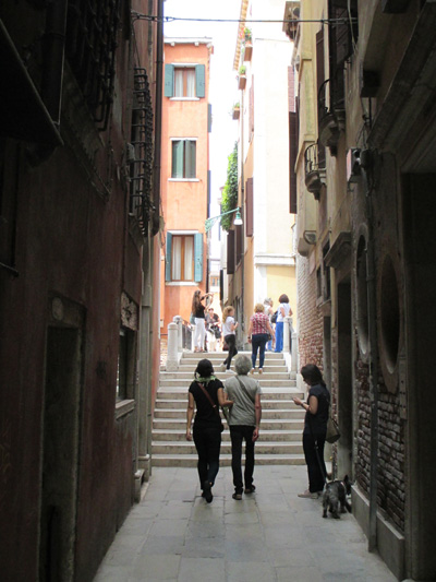 4 photos show an alley about 15 feet wide, with tables and chairs for a cafe along one side, and at the end of the buildings we see a set of stairs with about 7 steps going up.